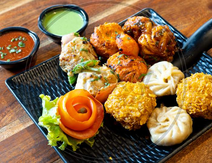 Tandoori Fried Roasted Momos Dimsum Pakora With Vegetable Flower Chicken And Green, White And Red Sauce Put In A Black Plate On A Wood Table