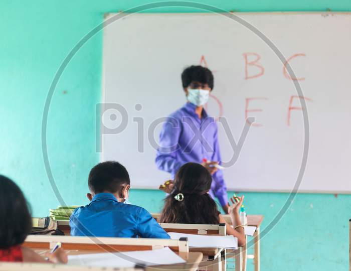 Focus On Middle Kid,Teacher In Medical Mask With Limited Kids Teaching At Classroom With Coronavirus Covid-19 Safety Measures At Classroom - Concept Of New Normal, Education And Back To School.