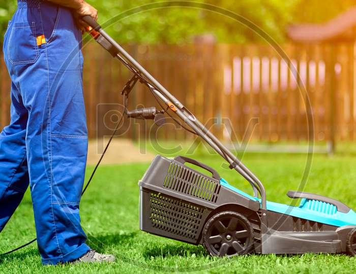 A Man With An Electric Lawn Mower Mowing The Lawn.Adult Man Pruning And Landscaping A Garden, Mowing Grass, Lawn, Paths.