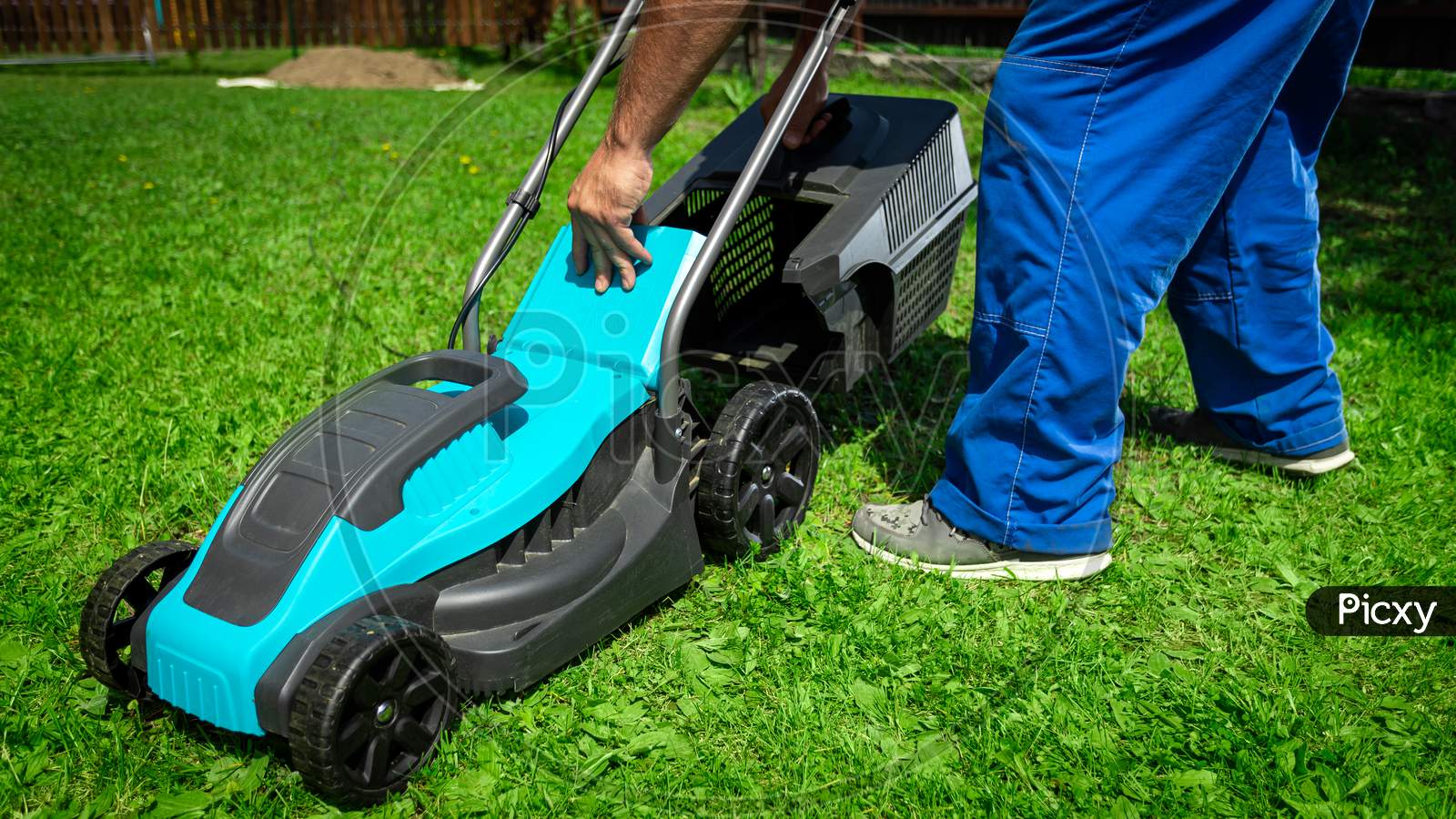 Lawn Grass Mowing. Worker Cutting Grass In A Green Yard. A Man With An Electric Lawn Mower Mowing A Lawn. Gardener Pruning A Garden