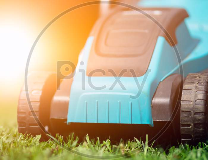 Male Worker On The Street Working On Mowing The Lawn With The Help Of A Modern Lawn Mower Near A Country House