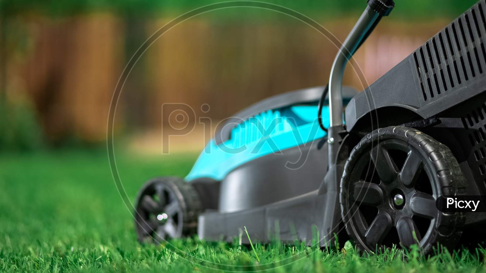 Lawn Grass Mowing. Worker Cutting Grass In A Green Yard. A Man With An Electric Lawn Mower Mowing A Lawn. Gardener Pruning A Garden