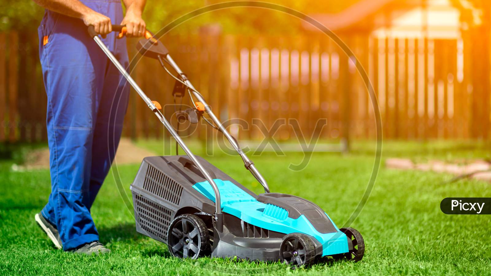 Lawn Grass Mowing. Worker Cutting Grass In A Green Yard. A Man With An Electric Lawn Mower Mowing A Lawn. Gardener Pruning A Garden
