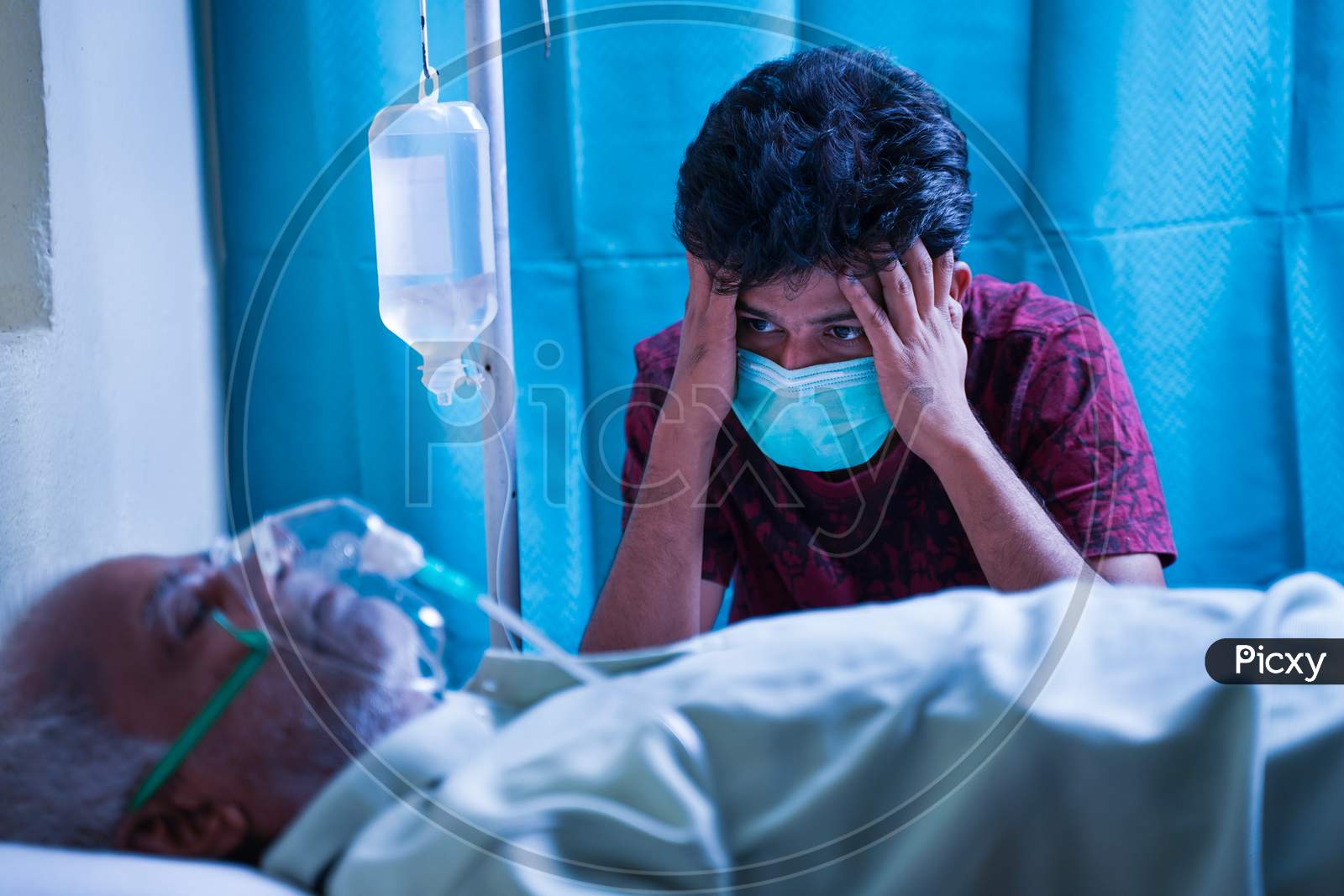 Worried Stressed Out Young Man Due To His Father Covid 19 Infection And Breathing On Ventilator Oxygen Mask At Hospital - Concept Of Mental Illness On Family Members Due To Coronavirus Pandemic.