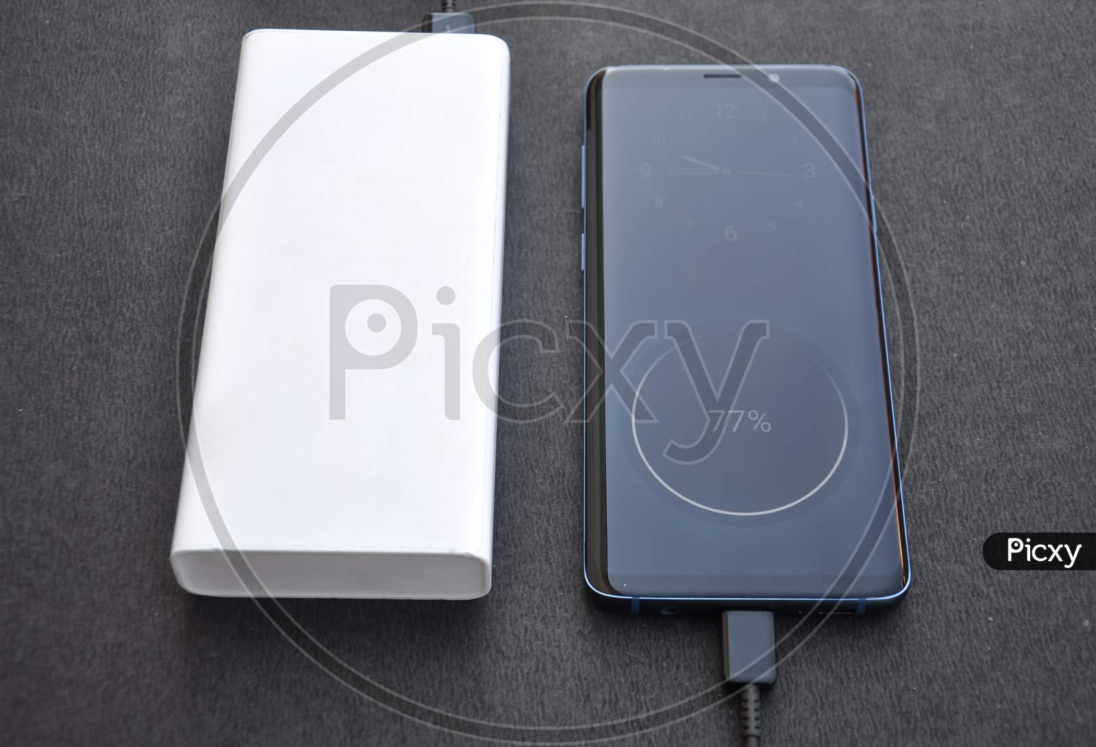 Photo of a black color smartphone connected with power bank for charge with black background