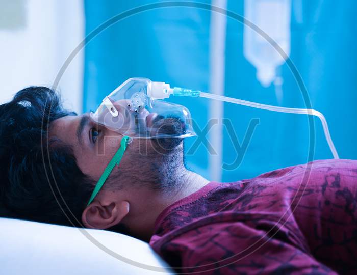 Side View On Young Man Breathing On Ventilator Oxygen Mask At Hospital Due Coronavirus Covid-19 Dyspnea Or Breathlessness - Concept Of Covid Infecting Millennial People.