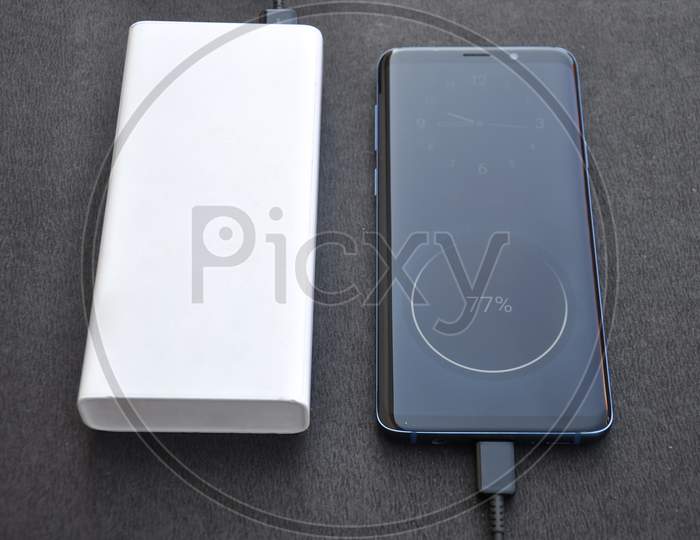 Photo of a black color smartphone connected with power bank for charge with black background