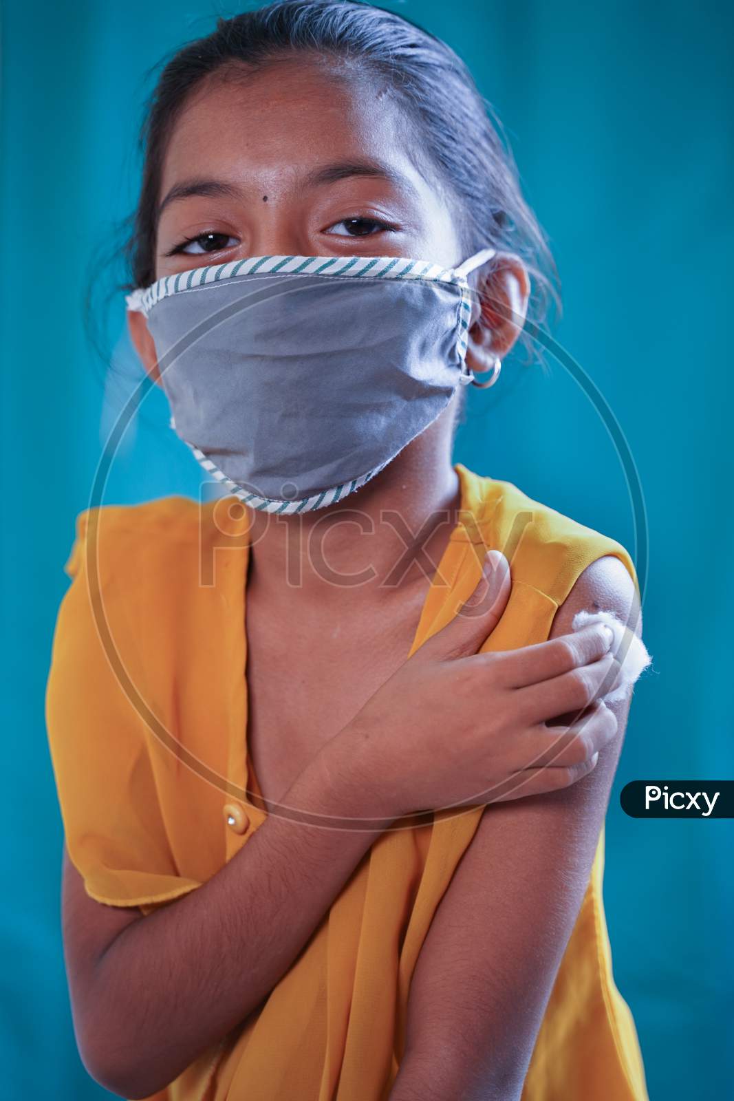 Portrait Of Covid Vaccinated Young Gril Kid With Medical Mask Looking Camera By Holding Arm - Concept Of Coronavirus Vaccination Trials For Children