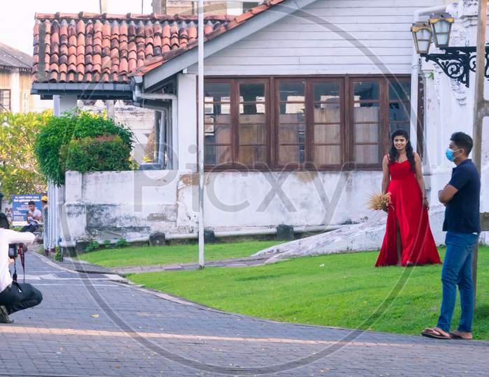 Galle, Sri Lanka - 02 12 2021: Streets Of Galle Fort, New Normal Concept, Beautiful Model In Red Frock Photoshoot In The Evening, Photographer In The Middle Of The Road Crouched.