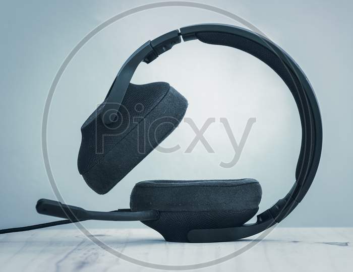 Black Gaming Headset With Detachable Cables, Microphone, And Adjustable Headband, The Concept Of Modern Technology, Headset Standing On An Ear Cup Side View.