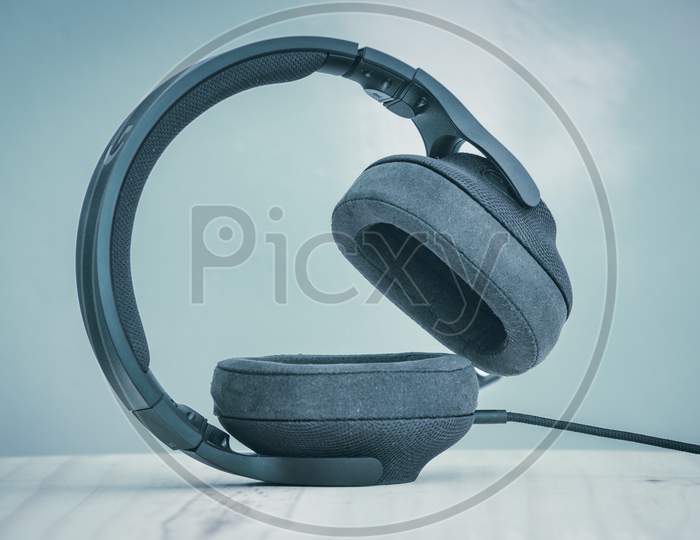 Black Gaming Headset With Detachable Cables, Microphone, And Adjustable Headband, The Concept Of Modern Technology, Headset Standing On An Ear Cup Side View.