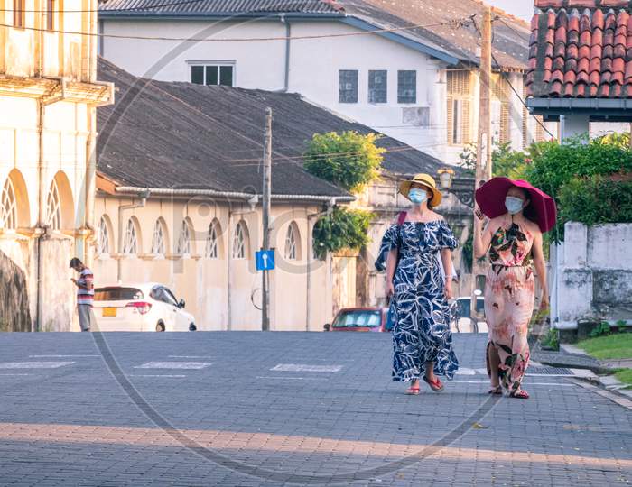 Galle, Sri Lanka - 02 12 2021: Two Female Tourists With Big Hats Walks In The Streets Of Galle Fort In The Evening, Enjoying The Beautiful View Of Colonial Age Built City. Interlock Blocks Street.