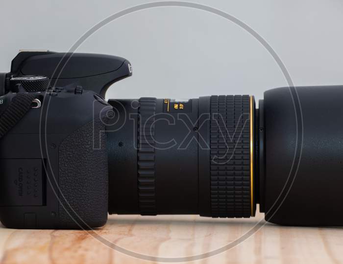 Modern Entry Level Dslr And Prime Lens Side View On A Wooden Table, Neck Strap And Lens Hood Attached,