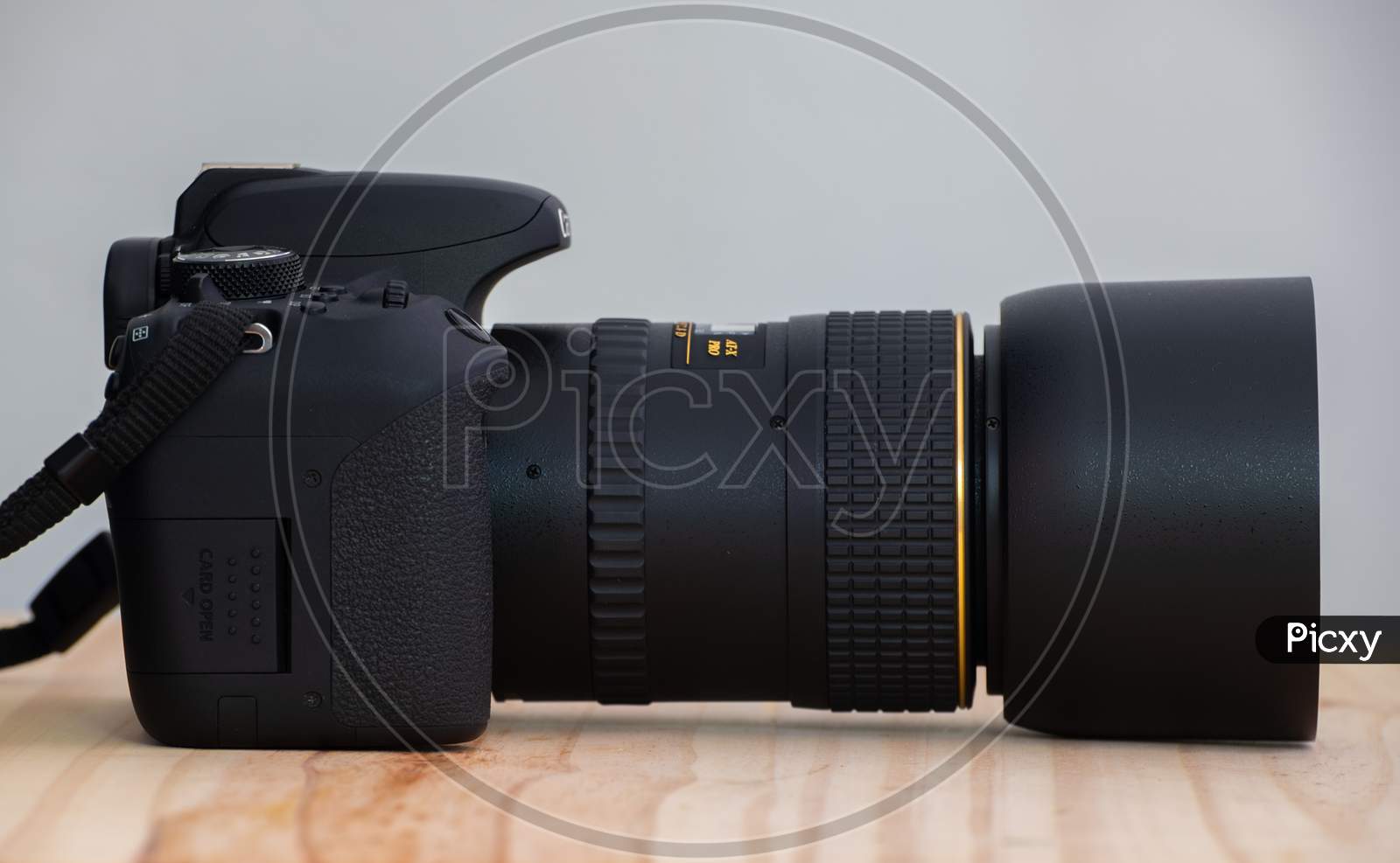 Modern Entry Level Dslr And Prime Lens Side View On A Wooden Table, Neck Strap And Lens Hood Attached,