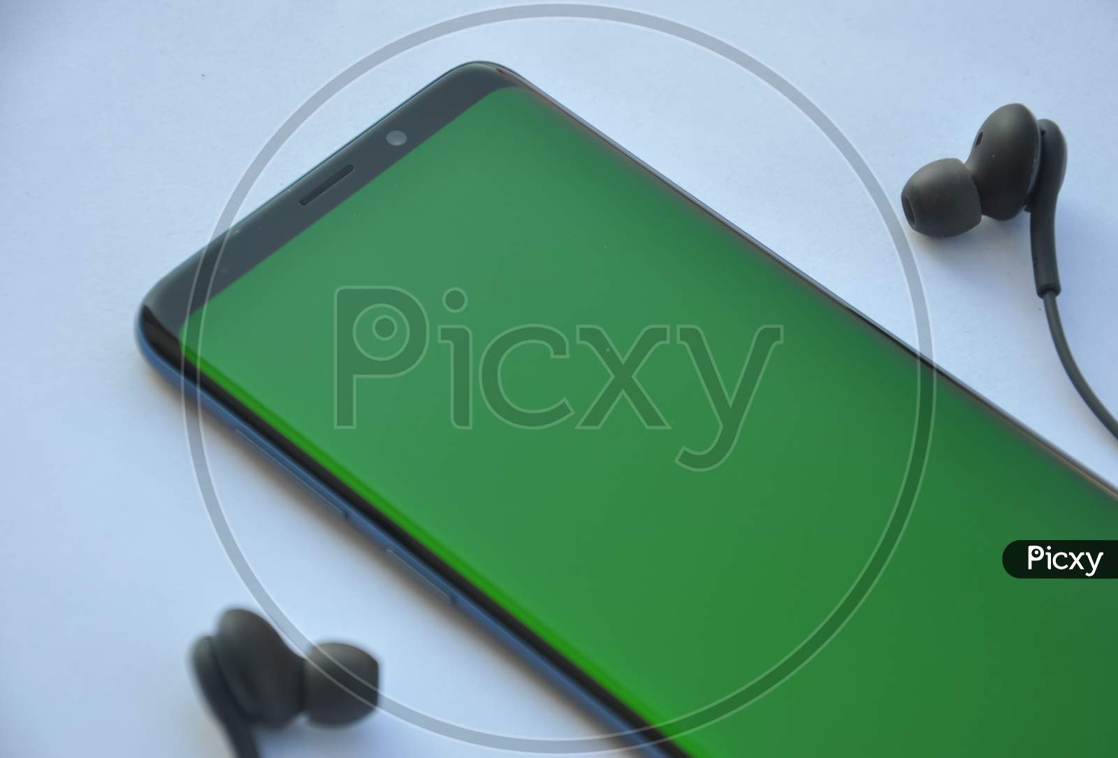 Low angle view of curved screen mobile phone with green screen and black color earphone over white background