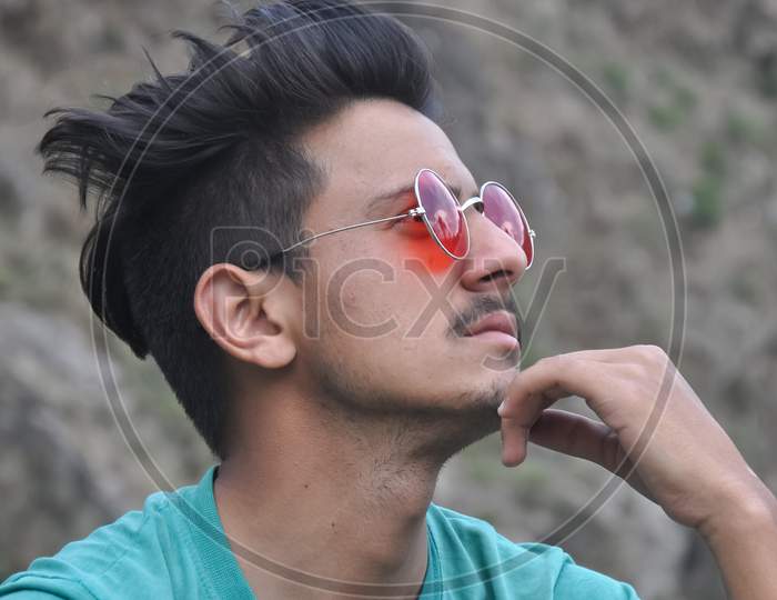 Closeup shot of a good looking young guy wearing sunglass sitting outdoor and his hand on chin with looking up, People thinking - Stock Photo