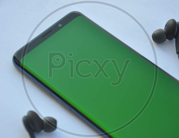 Low angle view of curved screen mobile phone with green screen and black color earphone over white background