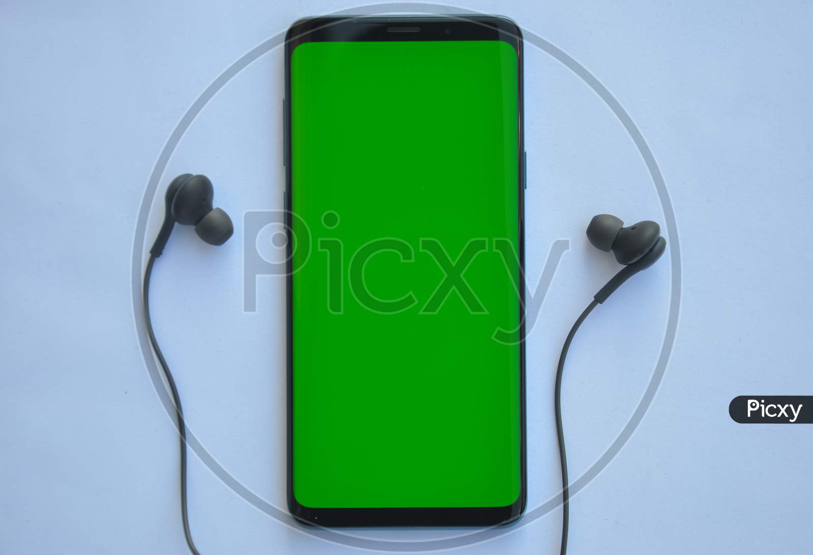 High angle shot of smartphone phone with green screen and black color earphone on top of white background