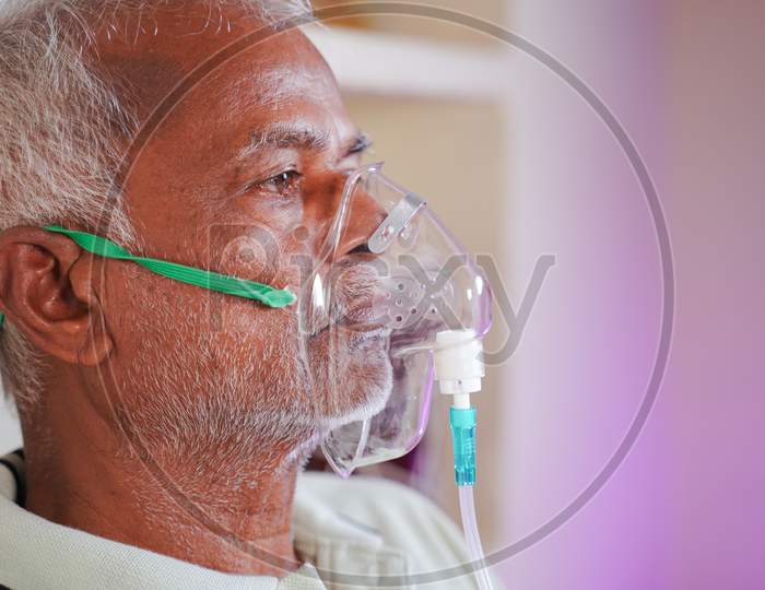 Close Up Head Shot Of Old Man Breathing On Ventilator Oxygen Mask At Home Due To Coronavirus Covid-19 Breathing Problem And Viral Infection