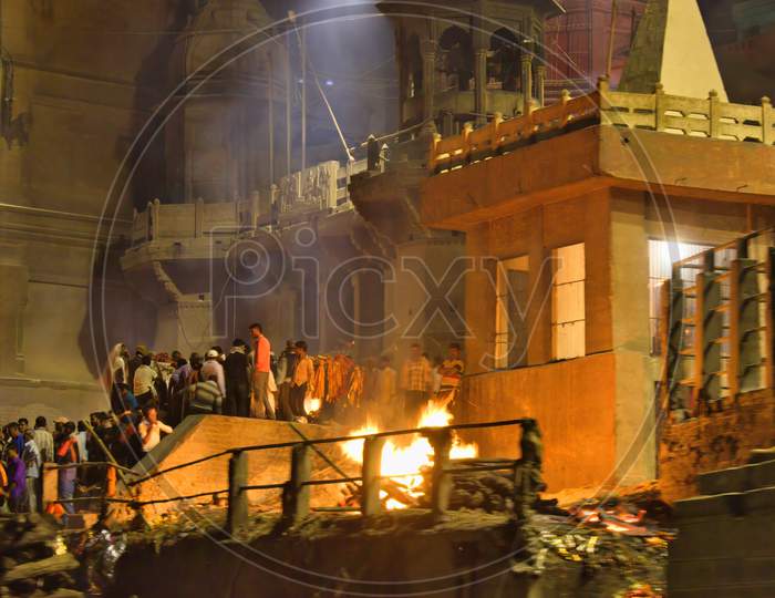 Varanasi, India - November 01,2016: View Of Holy Manikarnika Ganges River Ghat Of Banaras With Ancient City Architecture And Burning Piled Wooden Logs For Cremation At Night. Long Exposure Shot