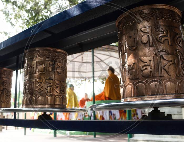Prayer Wheels Also Known As Dhamma Chakka Pavattana Sutta Wheel Of Law Against Buddha In Preaching Mode With His Disciples At Sarnath At The Sacred Buddhist Pilgrimage Site, Uttar Pradesh, India