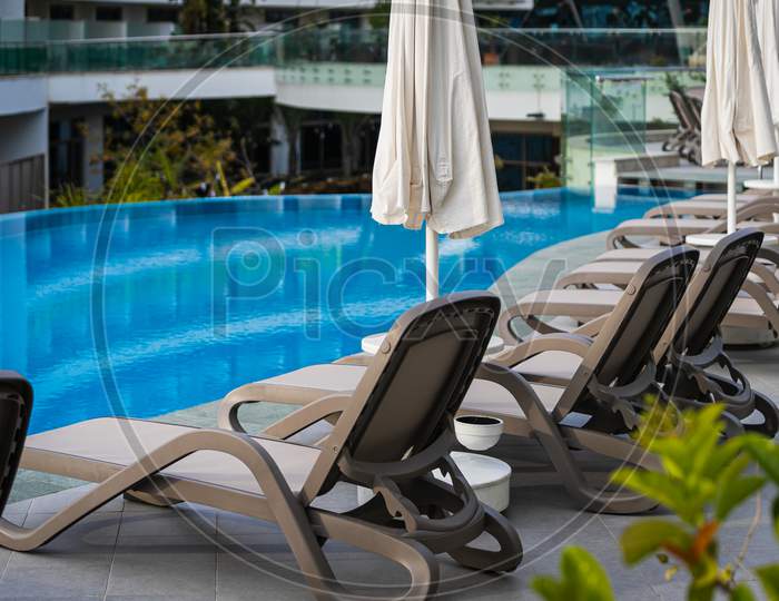A  Comfortable Gray Sun Loungers Set Against The Backdrop Of A Beautiful Transparent Pool And Hotel. The Concept Of A Relaxing Seaside Vacation