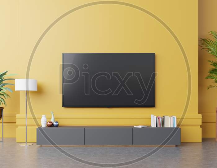 Tv On Cabinet In Modern Living Room With Lamp,Table,Flower And Plant On Yellow Wall Background.
