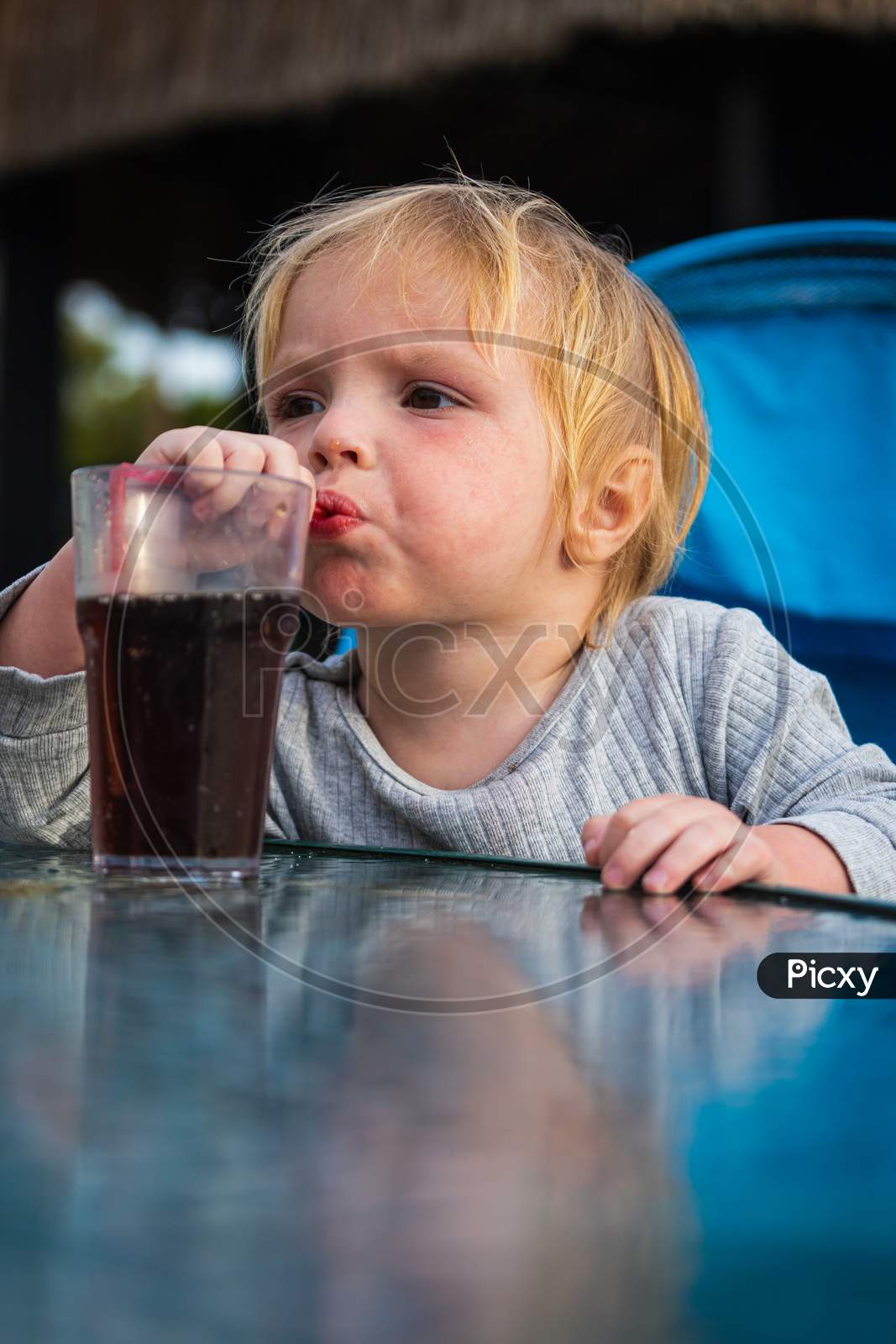 A Little Boy Is Sitting On A Chair And Happily Drinks Sparkling Water From A Glass Through A Straw. Feeding Process. The Baby Is Learning To Eat. Baby Food, Family, Child, Food