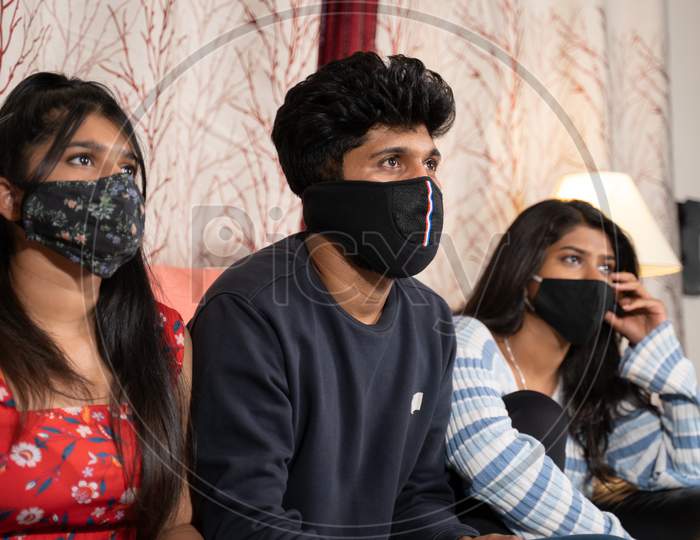 Siblings With Medical Face Mask Busy Watching Movie Or Online Webs Series Or Covid News While Sitting On Sofa During Lockdown Due To Coronaviru Covid-19 Pandemic.