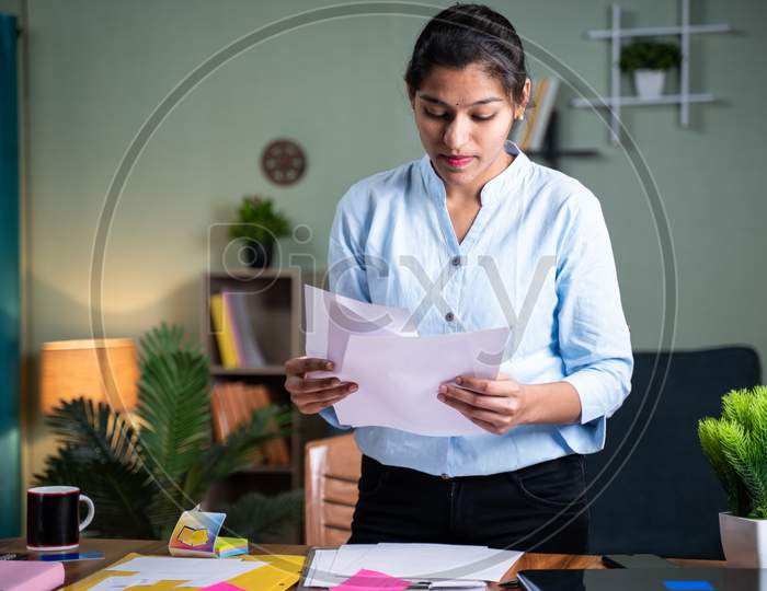 Standing Young Busy Woman Arranging Papers On Working Desk After Completion Of Work - Female Business Woman Busy Looking Documents At Home - Concept Of Wrk From Home During Coronavirus Lockdown.
