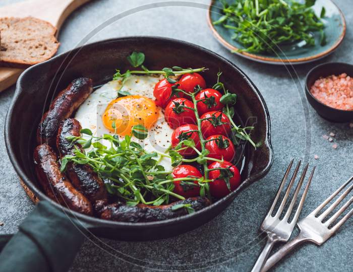 Breakfast Time, Fried Egg With Sausages And Cherry Tomatoes In A Black Iron Pan, Served Microgreens.