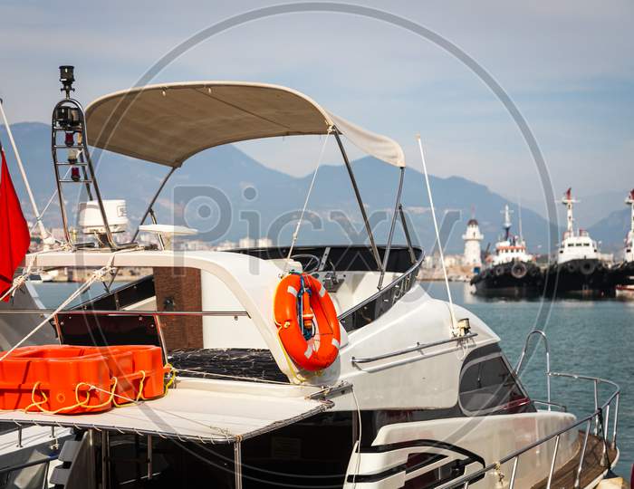 Wooden Side Of The Boat, Painted White And Brown, With A Orange  Lifebuoys  And Ropes Against The Background Of Sea Water