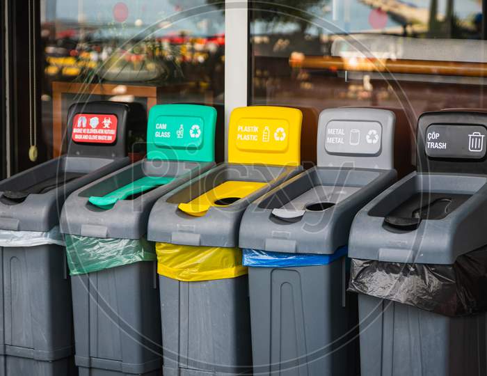 There Are Five Trash Cans On The Street: Red For Masks, Green For Glass, Yellow For Plastic And Packaging, Gray For Metal, And Black For Residual Waste. Garbage Sorting Concept.