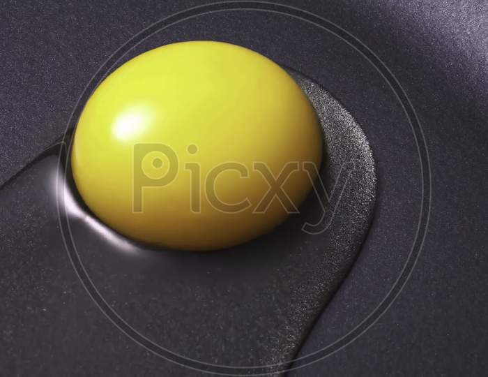Closeup of raw yellow egg yolk on a black frying pan.