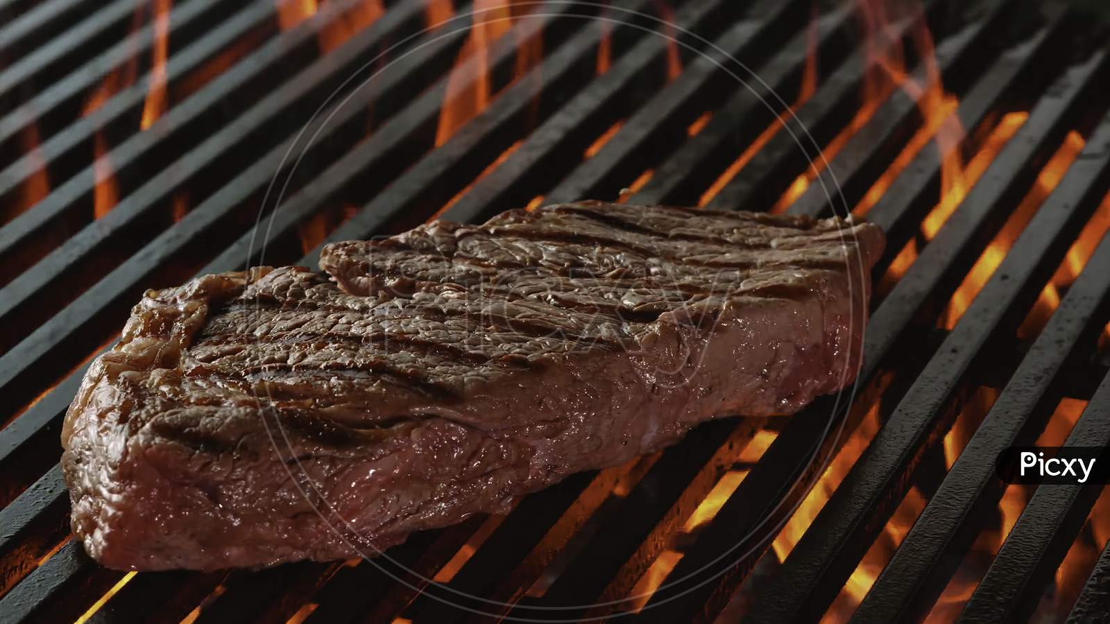 beef steak on the grill with flames.. A thick strip steak being grilled outdoors.