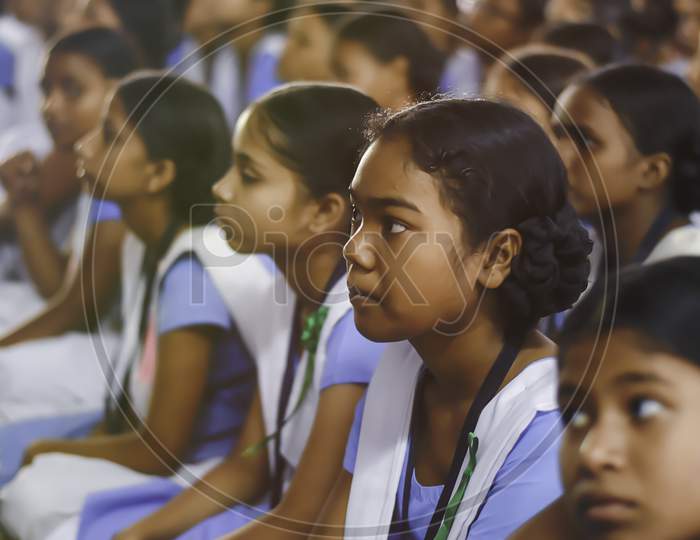 Indian school girl student in uniform. School students sitting on floor studying inside classroom.