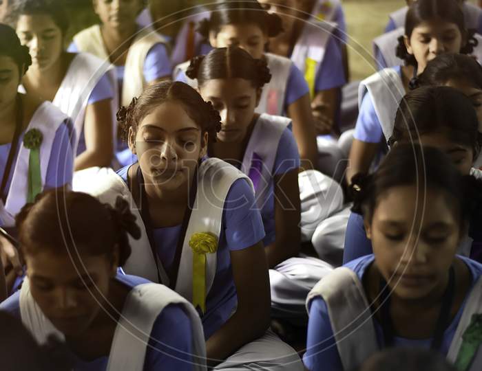 Young school girls in uniform sitting on floor, eyes closed learning and memorizing lessons inside class room of a government school.