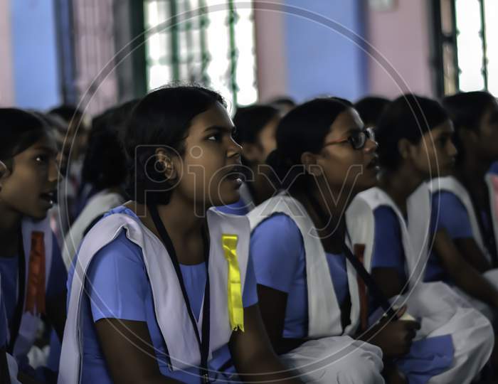Indian school girl student in uniform. School students sitting on floor studying inside classroom.