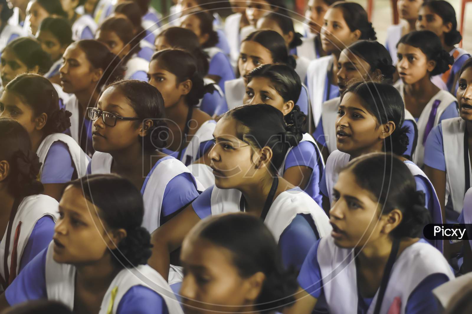 Indian school girl student in uniform. School students sitting on floor studying inside classroom.