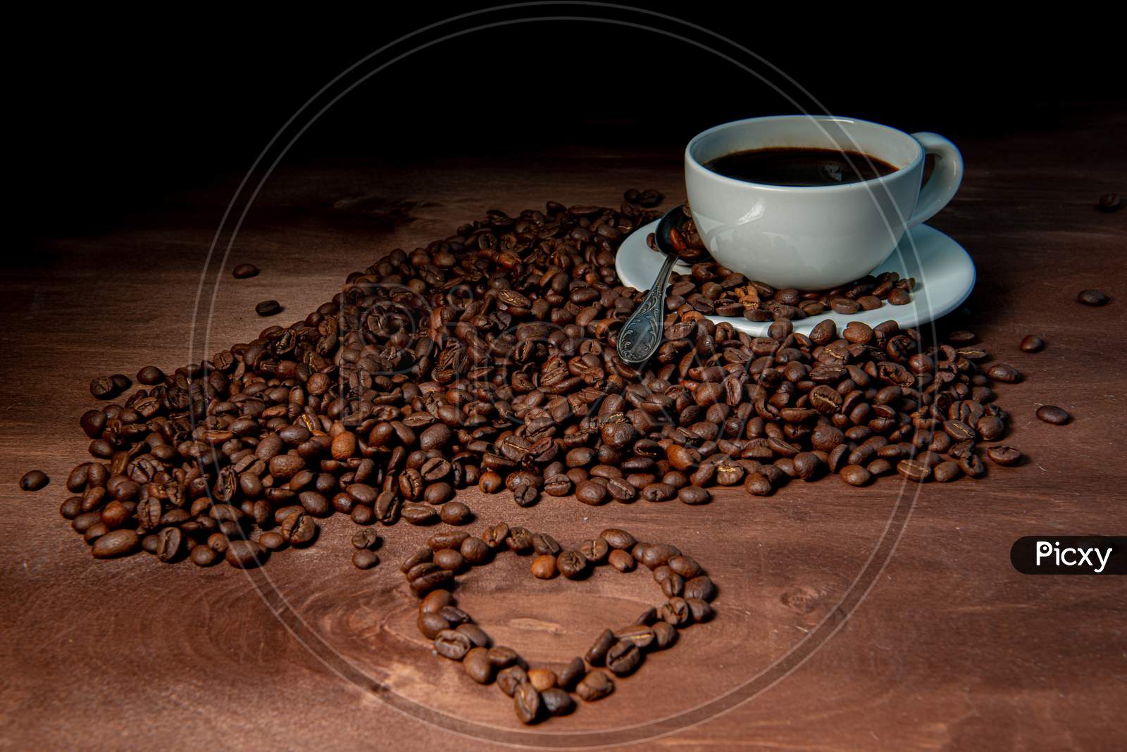 White Coffee Mug And Coffee Beans On The Dark Wooden Background, Heart Shape From Coffee Beans In The Foreground - Image