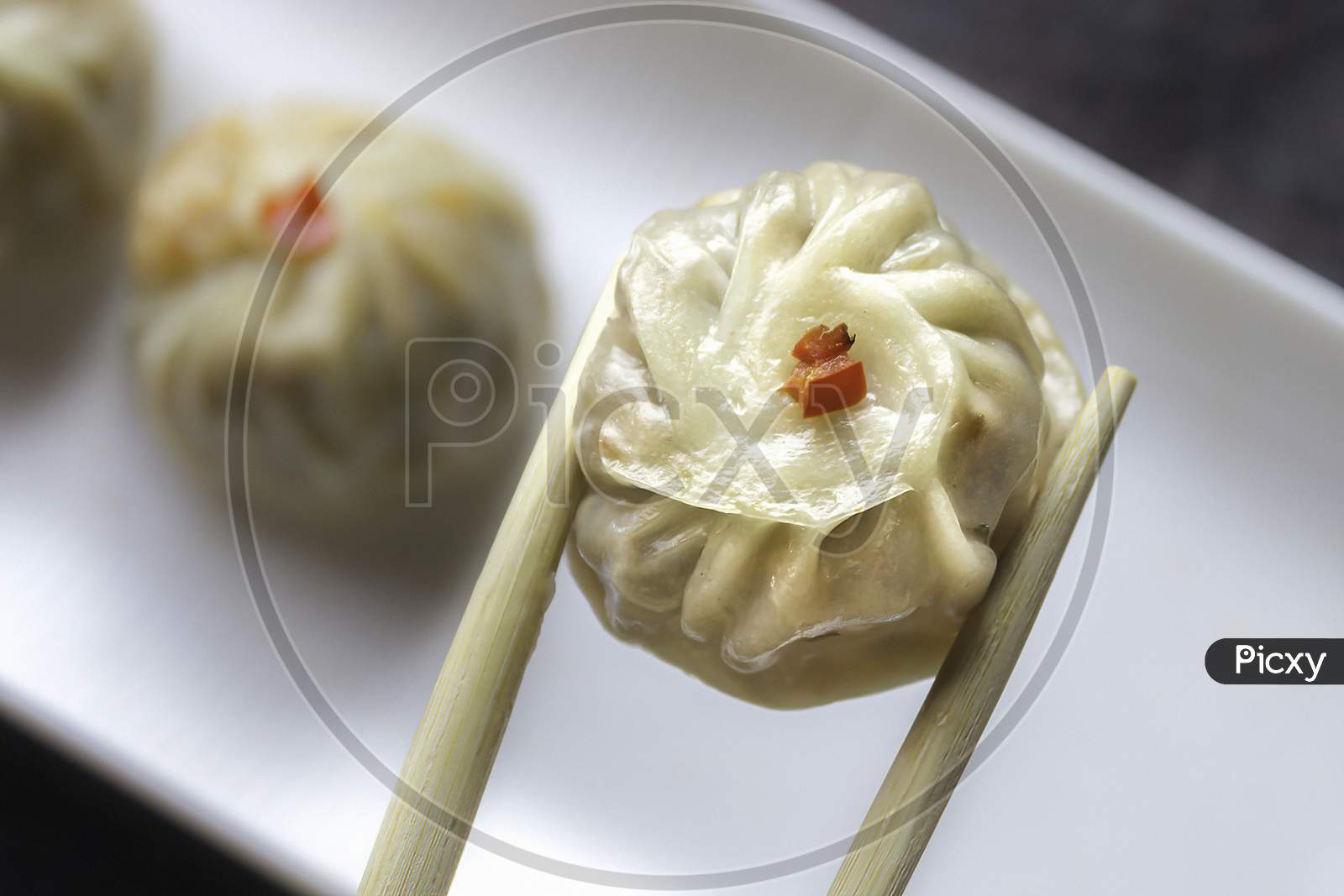 Close up fresh steamed momo dumpling with chopsticks. a piece of dimsum, clipped with chopsticks.