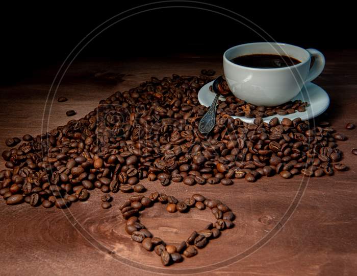 White Coffee Mug And Coffee Beans On The Dark Wooden Background, Heart Shape From Coffee Beans In The Foreground - Image