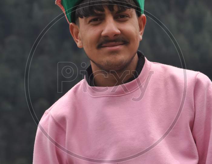 Portrait of a handsome young guy wearing pink color sweatshirt and himachali topi (Himachali traditional cap), A good looking north Indian young men standing outdoor with looking at camera