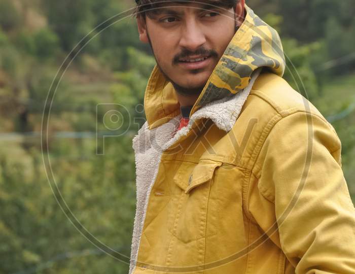 Side view of a handsome guy with hand on pocket and looking sideways, A good looking young guy wearing yellow jacket and himachali topi (Himachali traditional cap)