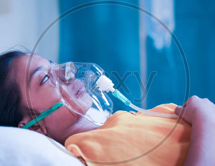 Side View Of Girl Kid Breathing On Ventilator Oxygen Mask Due To Coronavirus Covid-19 Breathing Shotness Or Dyspnea - Concept Of Children Healthcare And Medical During Third Wave Pandemic Outbreak.