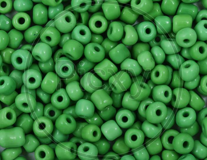 Green Beads On The White Background. Background Or Texture Of Beads. Close Up, Macro,It Is Used In Finishing Fashion Clothes. Make Bead Necklace Or String Of Beads For Woman Of Fashion.
