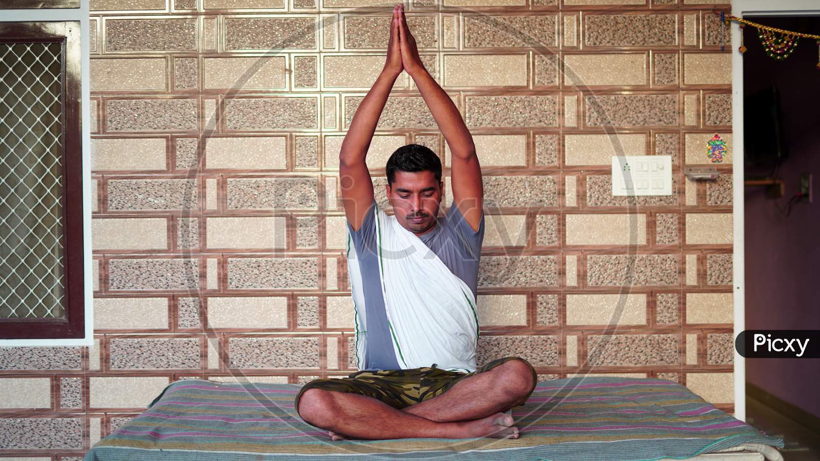 Young Indian Sitting In Yoga Position And Meditating At Home. Worldwide Yoga Day Concept.