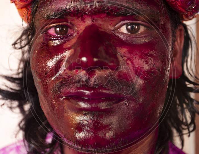 Indian man portrait with face smudged with multicolour and looking at camera