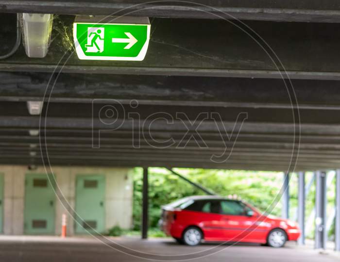 Green exit sign with running person and green arrow shows guidance system signage in a parking lot for rescue and evacuation safety in dangerous situations at ceiling to safe life in extreme danger