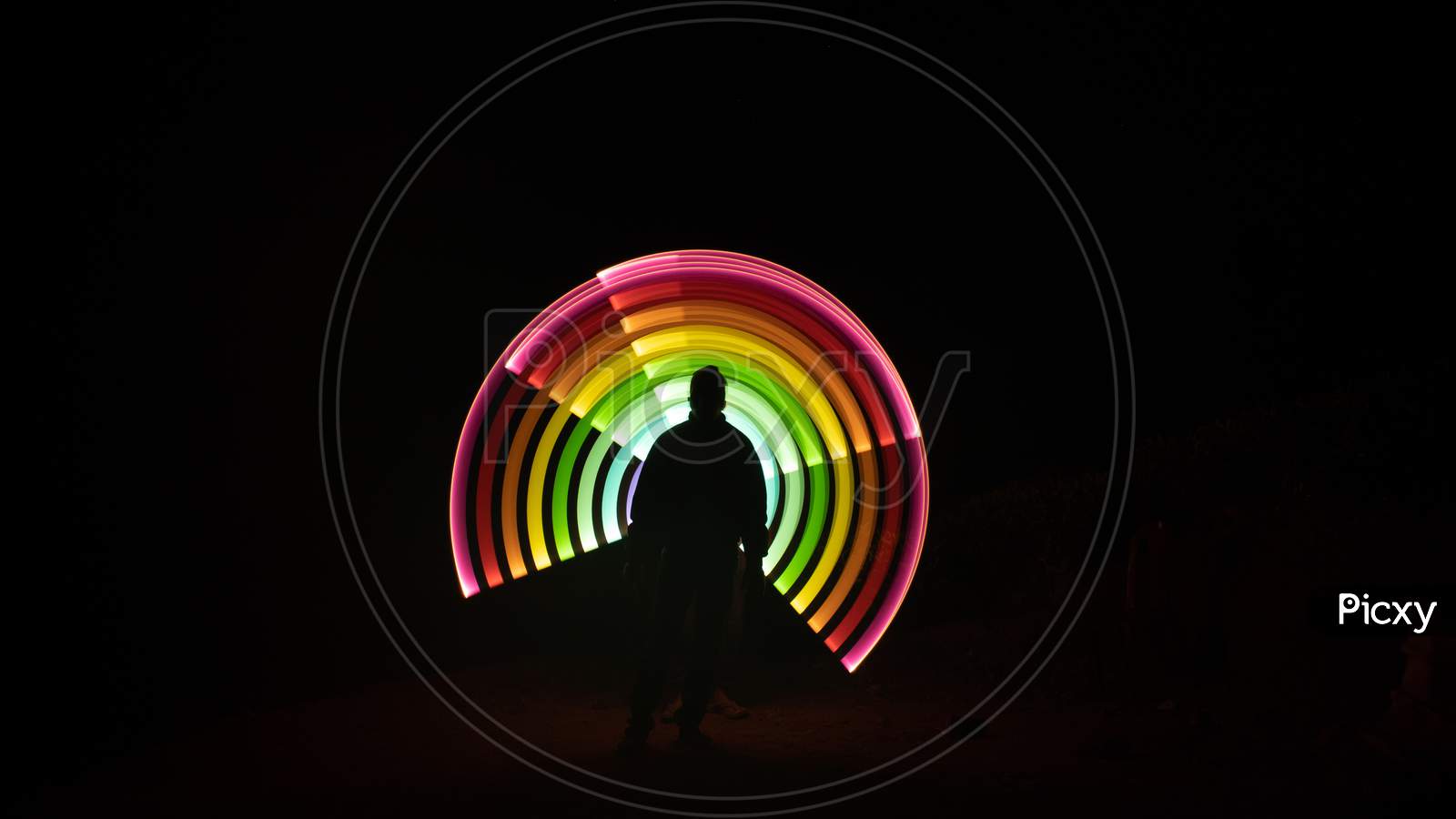 One Person Standing Against Beautiful Colorful Light Circle Light Painting As The Backdrop. Colorful Light Painting Portrait, Light Drawing At Long Exposure, Abstract Colorful Background
